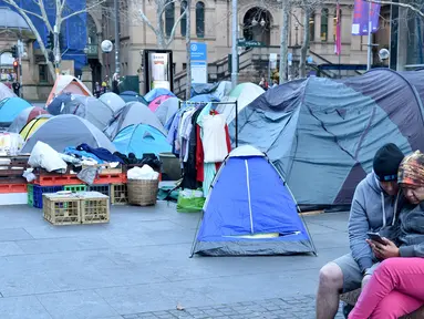 Pasangan tunawisma memainkan ponsel di depan perkampungan tenda para tunawisma di kawasan Martin Place, pusat kota Sydney, Rabu (9/8). Sydney kini tak hanya dipenuhi gedung bertingkat, tetapi juga disesaki tenda-tenda tunawisma. (PETER PARKS / AFP)