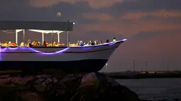 Pengunjung menikmati hidangan pada senja hari di sebuah restoran berbentuk perahu, tepi pantai Kota Gaza, Jalur Gaza, Rabu (2/8). Di restoran unik itu, pengunjung bisa menikmati lezatnya makanan sambil melihat matahari tenggelam. (MOHAMMED ABED / AFP)