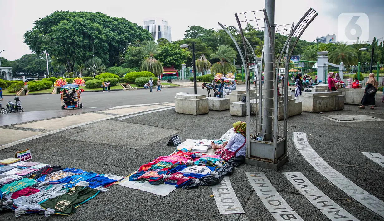 Pedagang kaos cendera mata keliling berjualan di kawasan Monas, Jakarta, Sabtu (2/1/2021). Meskipun Tugu Monas masih ditutup sejak awal pandemi Covid-19 tahun 2020, semangat para pedagang untuk berjualan tak pernah pudar. (Liputan6.com/Faizal Fanani)