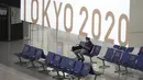 Sorang pria yang mengenakan masker pelindung untuk membantu mengekang penyebaran virus corona berhenti di dekat spanduk Olimpiade Tokyo 2020 di Bandara Internasional Narita, Tokyo, Selasa siang (1/6/2021). (AP Photo/Eugene Hoshiko)