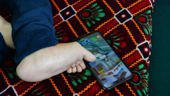 Seniman Robaba Mohammadi menggunakan ponsel dengan jari kaki di studionya di Kabul pada 5 Desember 2019. Meski terlahir dengan kaki dan tangan yang tidak bisa digunakan serta tak mendapatkan akses pendidikan, Robaba mampu membuat lukisan yang terbilang rumit dan penuh warna. (NOORULLAH SHIRZADA/AFP)