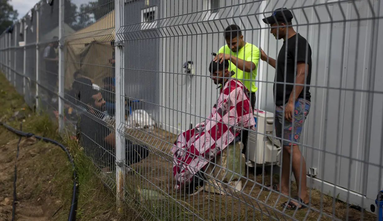 Para migran saling merapikan rambut di dalam kamp pengungsi di tempat latihan militer Rudninkai, Lituania, Rabu (4/8/2021). Lithuania, anggota Uni Eropa, telah menghadapi lonjakan sebagian besar migran Irak dalam beberapa bulan terakhir. (AP Photo/Mindaugas Kulbis)