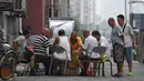 Sekelompok pria bermain kartu remi di trotoar di luar gedung apartemen di Beijing, China (10/8). Kartu remi, adalah sekumpulan kartu seukuran tangan yang digunakan untuk permainan kartu. (AFP Photo/Greg Baker)