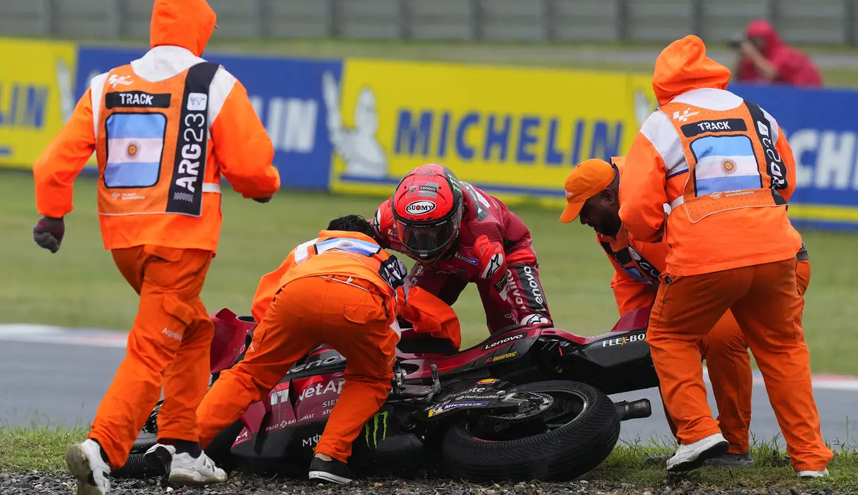 Terpleset dan tidak terlalu parah, Francesco Bagnaia berusaha mengangkat motornya dibantu beberpa orang petugas. (AP Photo/Natacha Pisarenko)