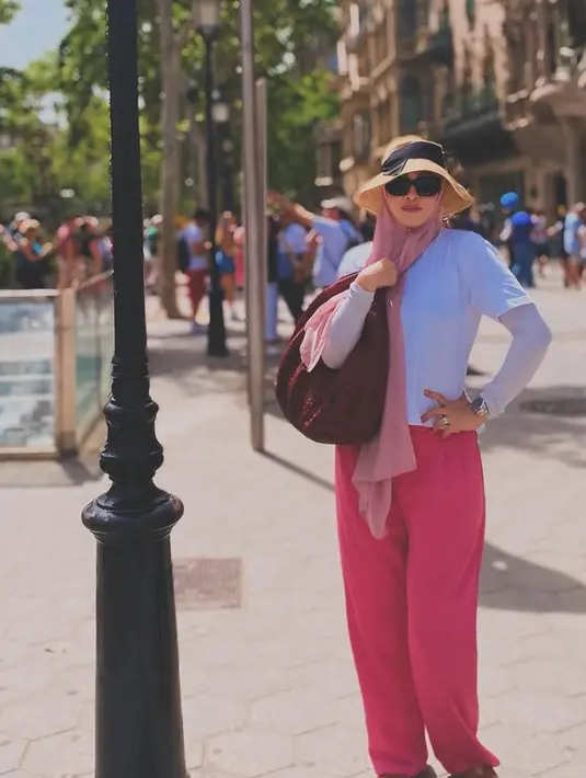 Jalan-jalan di Barcelona, Angelina tampil santai dengan kaos lengan pendek putih dipadukan manset abu-abu, serta kerudung panjang pink dan celana panjangnya. Sambil mengenakan topi ala ontau dan kacamata hitam. [@angelinasondakh09]