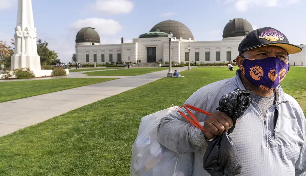 Jose Cartamo (64) dari El Salvador, memakai masker saat mengumpulkan barang daur ulang di Griffith Observatory di Los Angeles, Senin (17/5/2021). California mempertahankan aturan untuk mengenakan masker hingga negara bagian itu mencabut pembatasan COVID-19 pada 15 Juni. (AP Photo/Damian Dovarganes)