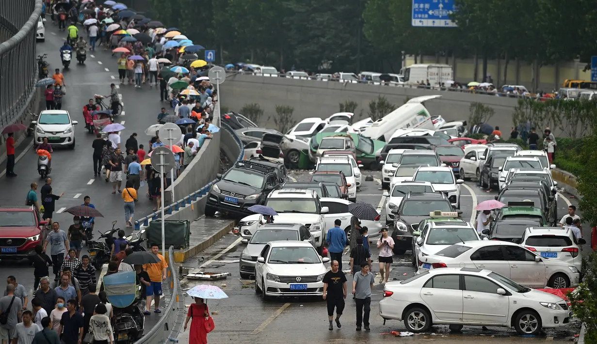 Orang-orang melihat mobil-mobil yang terendam banjir setelah hujan lebat di Zhengzhou, provinsi Henan, China, Kamis (22/7/2021). Hujan yang membanjiri jalan-jalan membuat pengendara terpaksa menempuh banjir setinggi pinggang yang menenggelamkan atau menghanyutkan banyak mobil. (Noel Celis/AFP)