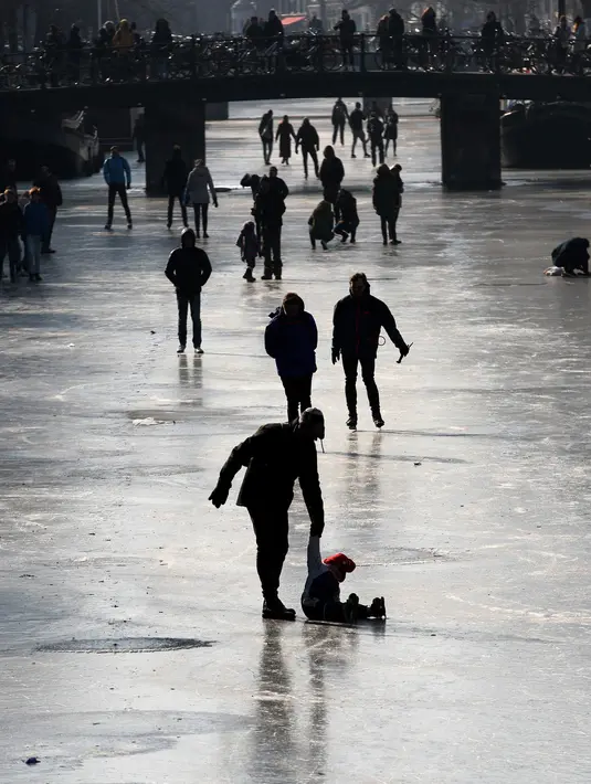 Orang-orang berseluncur dan berjalan melintasi permukaan kanal Prinsengracht yang membeku di Amsterdam, Belanda, Jumat (2/3). Lapisan kanal yang membeku cukup tebal untuk menahan beban ratusan warga yang datang. (AP/Mike Corder)