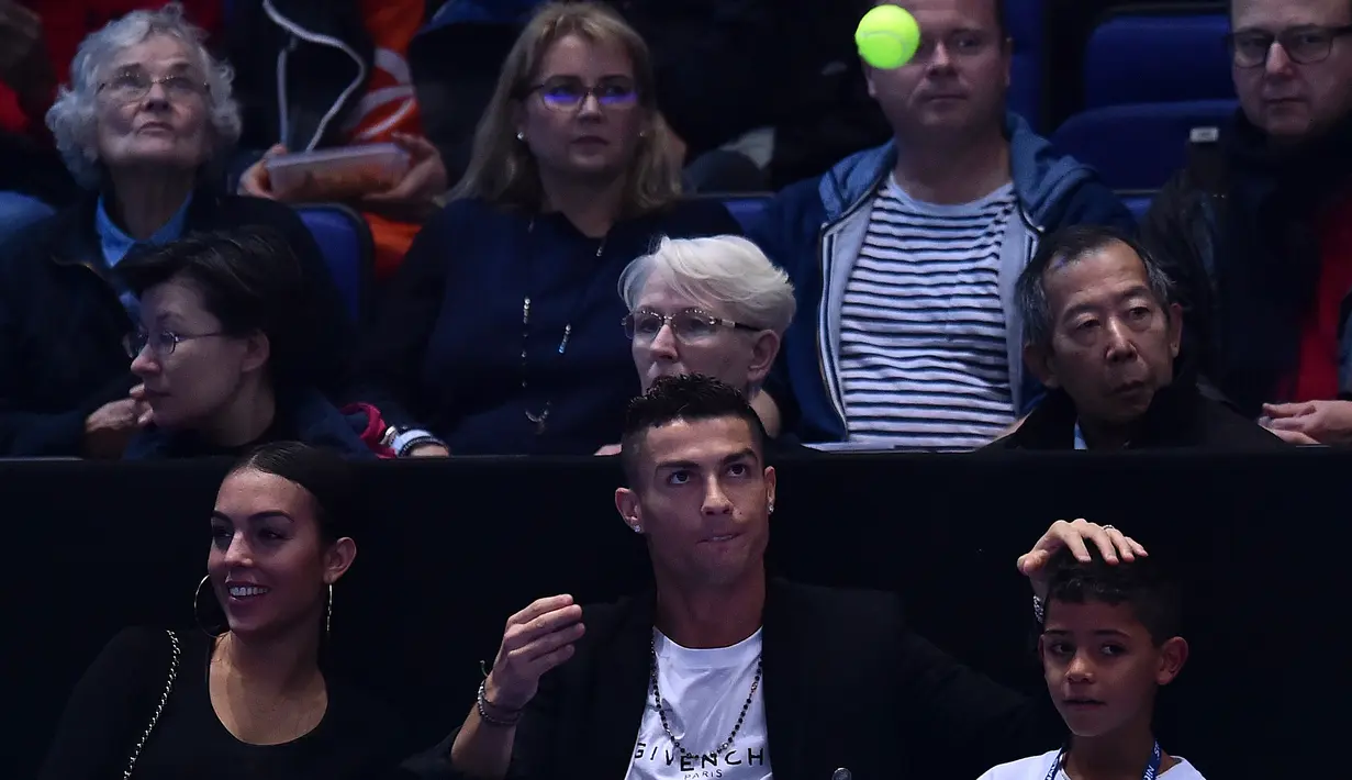 Pemain Juventus, Cristiano Ronaldo mengembalikan bola tenis yang mengarah kepadanya dan sang kekasih, Georgina saat menyaksikan Novak Djokovic menghadapi John Isner pada laga tenis dunia, ATP Finals 2018 di O2 Arena, London, Senin (12/11). (Glyn KIRK/AFP)