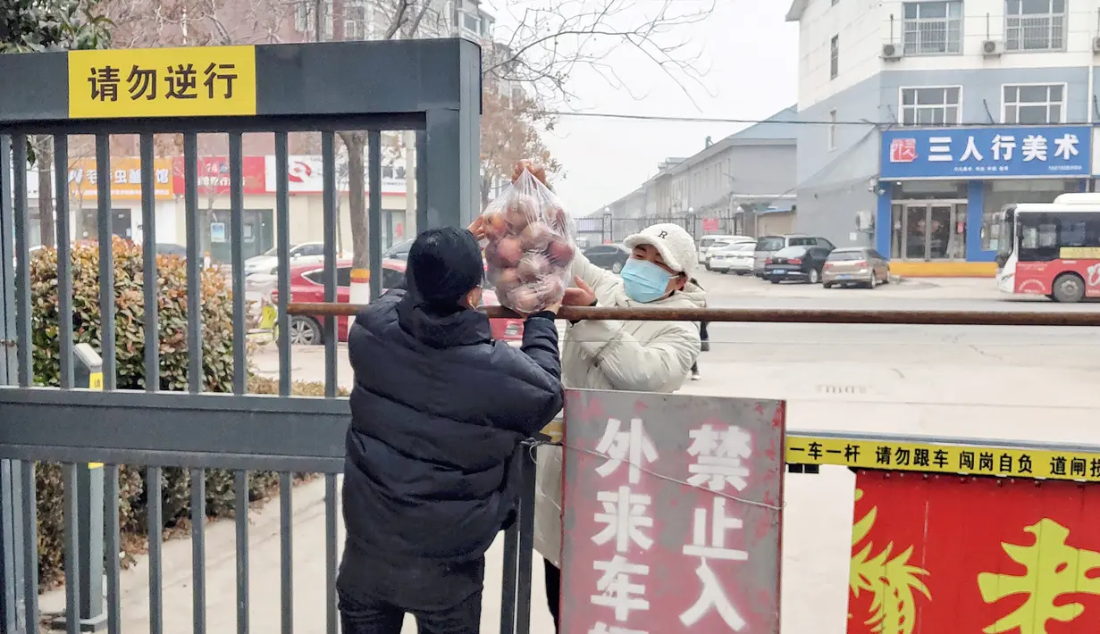 Seorang penduduk menerima makanan di pintu masuk area perumahan yang ditutup dan dibatasi karena pandemi Covid-19 di Anyang provinsi Henan, 12 Januari 2022. China sedang berjuang melawan covid di beberapa kota, beberapa minggu sebelum Beijing menjadi tuan rumah Olimpiade Musim Dingin 2022 (STR/AFP)