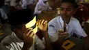 Pelajar menjajal kacamata filter buatan sendiri dengan cahaya senter ponsel dalam workshop di sebuah sekolah di Ternate, (7/3). Kacamata ini akan digunakan untuk mengamati Gerhana Matahari Total. (REUTERS/Beawiharta)