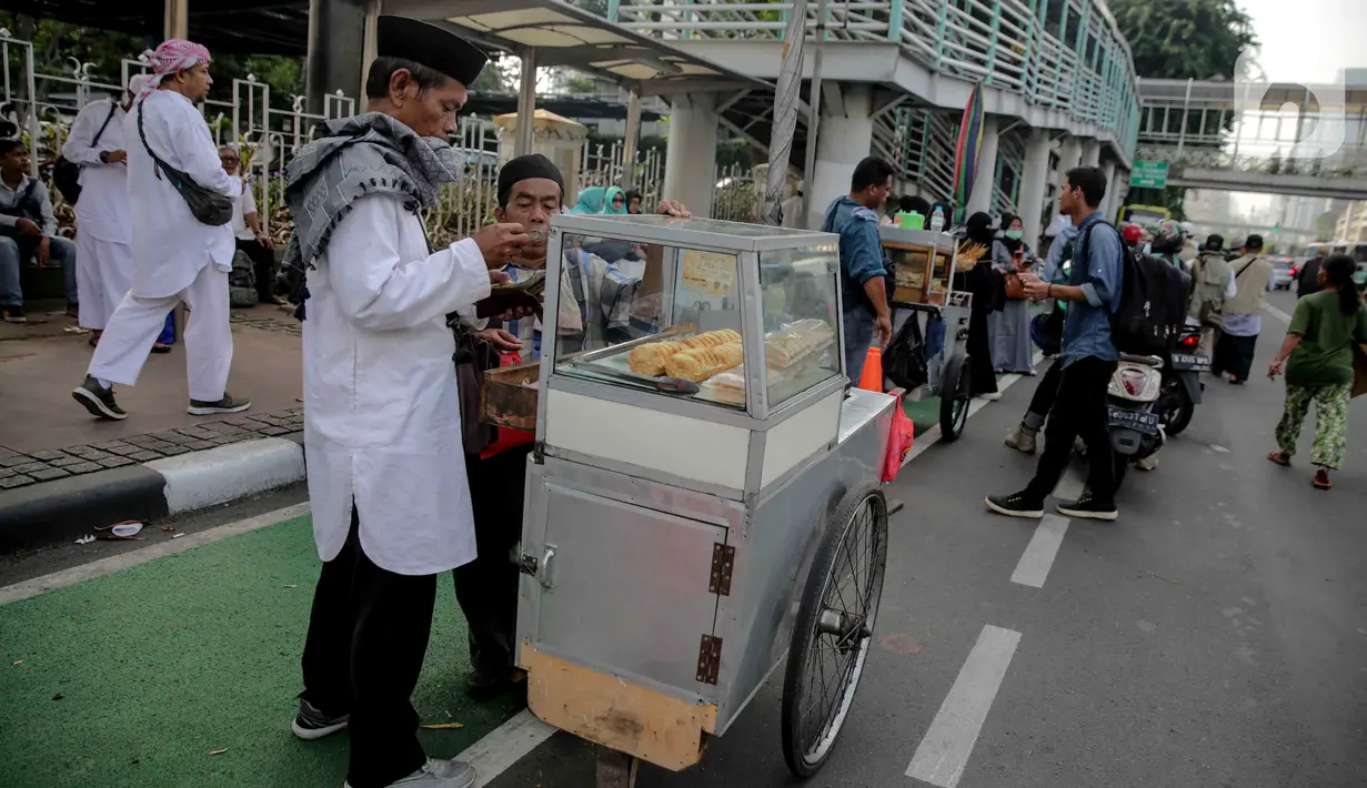 Pedagang makanan melayani pembeli saat berjualan di tengah aksi reuni 212, sekitaran Jalan Medan Merdeka Barat, Jakarta, Senin (2/12/2019). Sejumlah PKL meraup untung dengan berjualan di tengah ribuan massa Persaudaraan Alumni 212 yang mengikuti reuni di Monas. (Liputan6.com/Faizal Fanani)