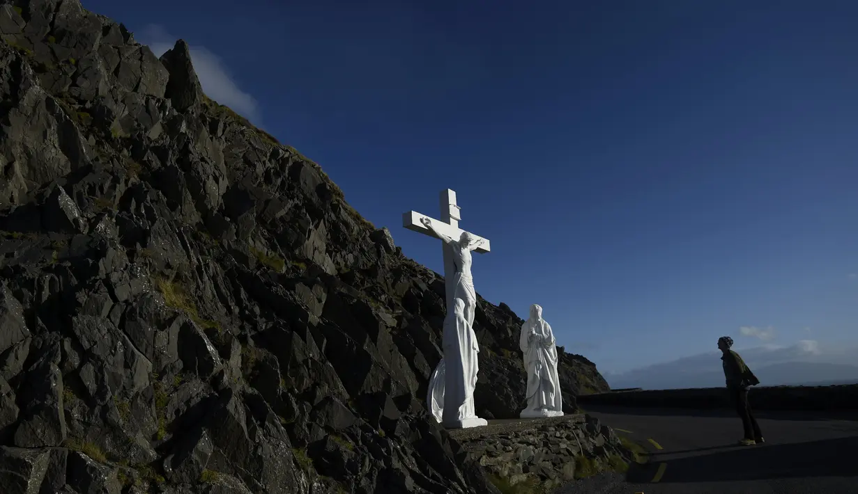 Seorang pria melihat patung penyaliban Kristus di atas tebing di Slea Head jalan di Ventry, Irlandia, Selasa (27/12). Irlandia mendapat julukan Pulau Zamrud karena memiliki pemandangan alam yang hijau terang. (REUTERS / Clodagh Kilcoyne)