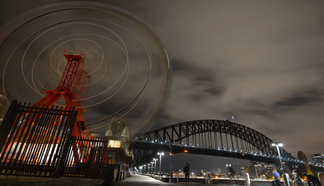 Ferris wheel di Park Luna dan Sydney Harbour Bridge terlihat padam tanpa lampu penerangan saat peringatan Earth Hour Internasional di Sydney, Austalia (25/3). (AFP/Peter Parks)