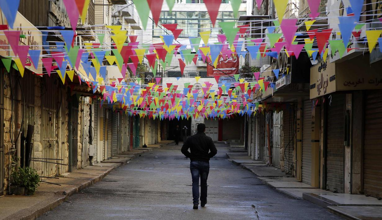 Seorang pria Palestina berjalan melewati toko-toko yang tutup di kota Nablus, Tepi Barat, (7/12). Usai Presiden AS, Donald Trump mengumumkan Yerusalem sebagai ibu kota Israel suasana sepi terlihat di kawasan tersebut. (AFP Photo/Jaafar Ashtiyeh)