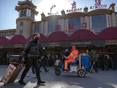 Wisatawan yang mengenakan masker untuk melindungi dari penyebaran virus corona berjalan dengan membawa barang bawaan mereka di Stasiun Kereta Api Beijing di Beijing, Kamis (28/1/2021).  Upaya untuk mencegah warga Tiongkok bepergian untuk Tahun Baru Imlek tampaknya berhasil. (AP Photo/Mark Schiefelb