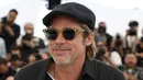 Aktor Brad Pitt tersenyum saat tiba menghadiri pemutaran film 'Once Upon a Time in Hollywood' selama Festival Film Cannes Internasional ke-72 di Prancis (22/5/2019).  Brad Pitt tampil santai mengenakan jeans hitam, kemeja polo hitam, kaca mata dan topi. (AP Photo/Vianney Le Caer)