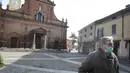 Seorang pria mengenakan masker berjalan di depan gereja San Biagio, Codogno, dekat Lodi, Italia Utara  (22/2/2020). Pihak berwenang Italia memerintahkan penutupan sekolah, bar, dan ruang publik lainnya di 12 kota, menyusul banyaknya kasus virus corona baru muncul di negara itu. (AP Photo/Luca Bruno)