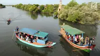 Perahu wisata melintasi kerumunan wisatawan yang berjalan di atas Jembatan Cinta di Wisata Mangrove, Tarumajaya, Bekasi, Minggu (30/12). Wisata tersebut awalnya merupakan Pusat Restorasi dan Pembelajaran Mangrove (PRPM) Bekasi. (merdeka.com/Arie Basuki)