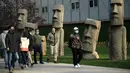 Orang-orang yang memakai masker berjalan melewati replika patung raksasa 'Moai' Pulau Paskah di Beijing pada Rabu (4/11/2020). Pulau Paskah yang berada di Negara Chile terkenal oleh patung kepala yang dipahat dari batu. (Photo by Noel Celis / AFP)