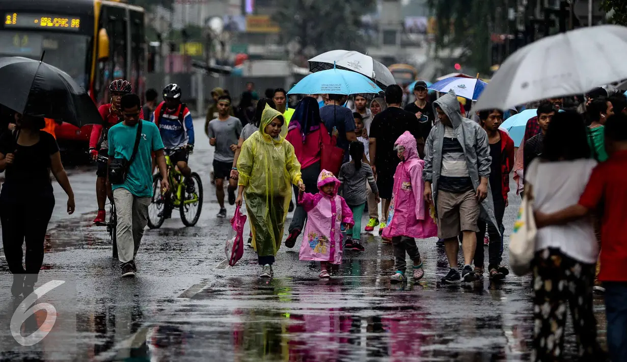 Sejumlah warga menggunakan jas hujan saat menghadiri Car Free Day di Bundaran HI, Jakarta, Minggu (13/11). Meski gerimis di kawasan tersebut mereka tak surut untuk berolahraga. (Liputan6.com/Faizal Fanani)