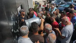 Warga Lebanon menunggu untuk mengisi tabung gas di kota selatan Sidon, Selasa (10/8/2021). Warga Lebanon harus mengantre panjang demi membeli gas untuk memasak di tengah krisis ekonomi parah yang memicu kelangkaan berbagai kebutuhan pokok dari obat-obatan hingga bahan bakar. (Mahmoud ZAYYAT/AFP)