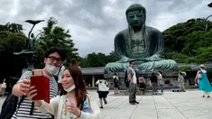 Sepasang pengunjung berswafoto dengan latar belakang The Great Buddha atau yang biasa disebut Kamakura Daibutsu di kuil Kotoku-in di Kamakura, Prefektur Kanagawa, Jepang, Sabtu (20/6/2020). Patung Buddha yang menjulang dengan tinggi 13,35 meter ini didirikan tahun 1252. (Behrouz MEHRI/AFP)