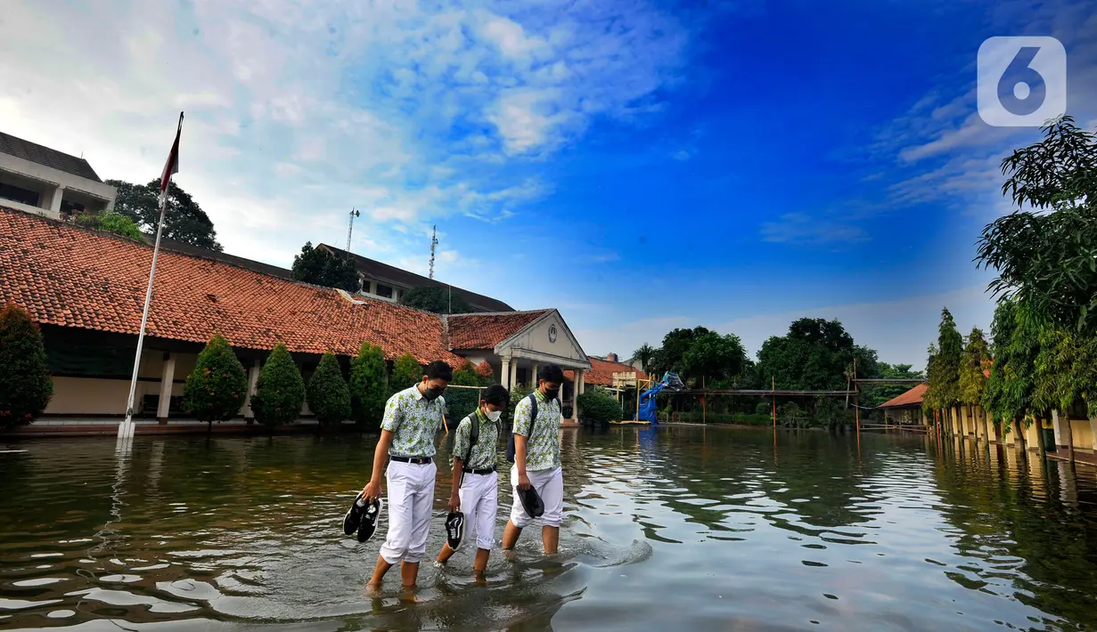 Siswa berjalan melewati banjir yang menggenangi halaman  sekolah di SMAN 4 Tangsel, Pondok Ranji, Tangerang Selatan, Banten, Selasa (14/6/2022). Tiga  pekan lebih banjir merendam lapangan sekolah itu dikarenakan tertutupnya saluran air oleh sampah yang berasal dari tempat pembuangan sampah (TPS) ilegal. (merdeka.com/Arie Basuki)
