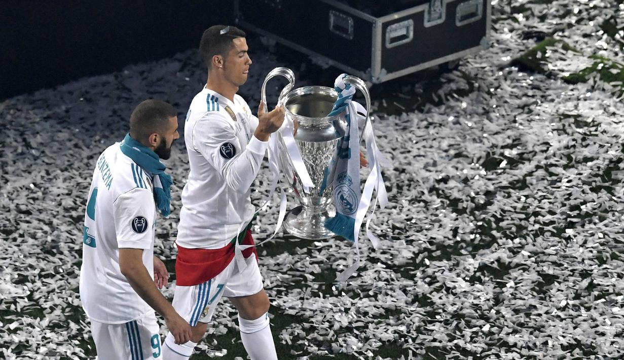 Pemain Real Madrid, Cristiano Ronaldo (kanan) membawa trofi Liga Champions 2017/2018 bersama rekannya Karim Benzema saat merayakan kemenangan di Stadion Santiago Bernabeu, 27 Mei 2018. (AFP/Gabriel Bouys)