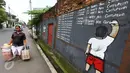 Seorang wanita melintas di depan mural anti korupsi bertuliskan 'I promise i'll learn not corruption' di Jakarta, Minggu (05/03). Mural tersebut mengedukasi masyarakat untuk belajar tidak melakukan praktik korupsi. (Liputan6.com/Helmi Afandi)