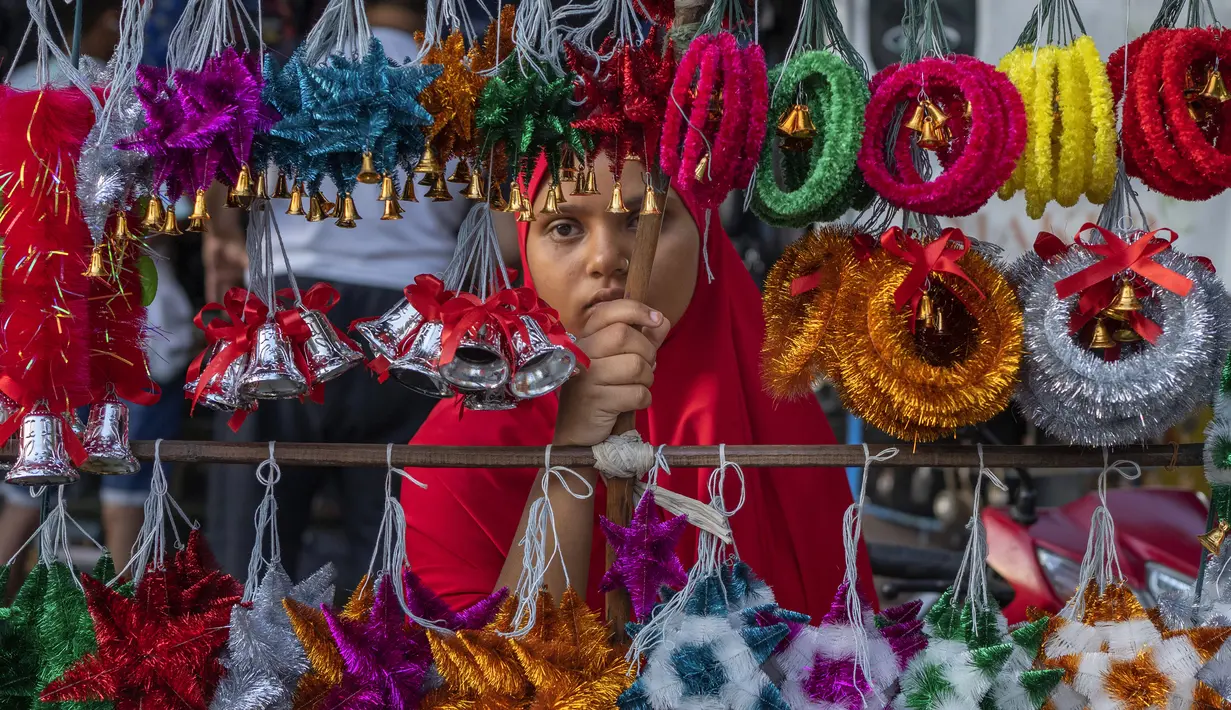 Seorang gadis penjual suvenir Natal menunggu pembeli di Mumbai, India, Selasa (20/12/2022). Jelang puncak perayaan Natal, warga Mumbai mulai ramai berburu ornamen dan aksesoris Natal untuk menyambut dan memeriahkan perayaan untuk umat kristiani tersebut. (AP Photo/Rafiq Maqbool)