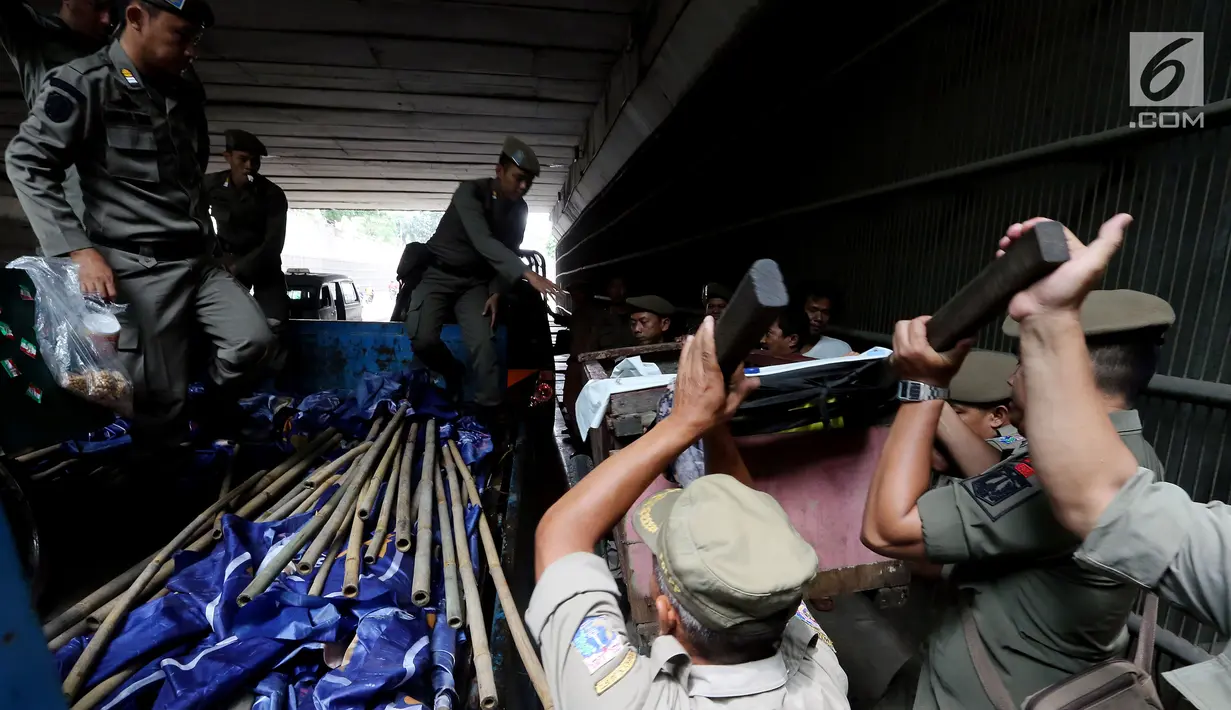 Petugas Satpol PP dari Kecamatan Setia Budi mengangkat gerobak tunawisma yang terjaring razia di Kawasan Kuningan, Jakarta, Rabu (15/11). Razia ini bertujuan untuk mengurangi dan memberantas penyakit masyarakat. (Liputan6.com/JohanTallo)