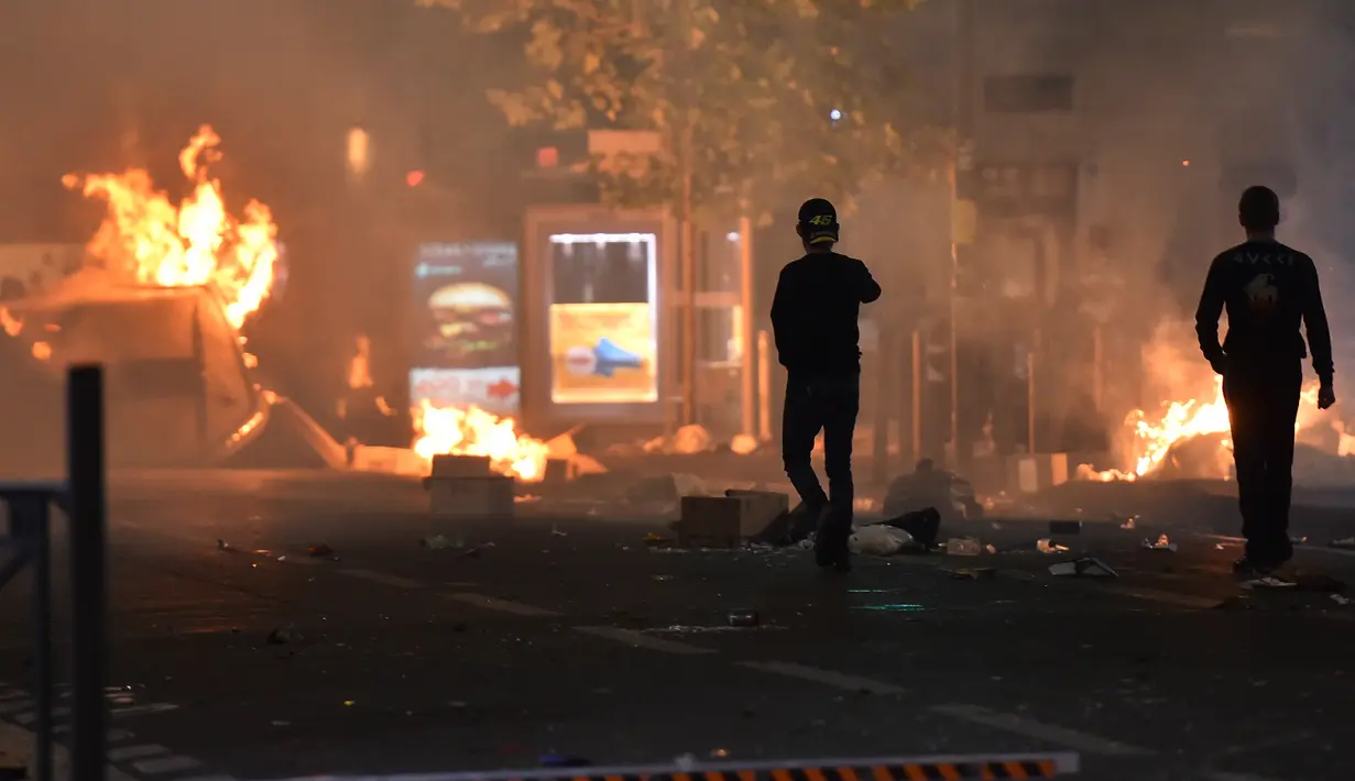 Dua orang berjalan di dekat api saat terjadi kericuhan yang disebabkan oleh pendukung Marseille di Vieux Port di Marseille, Prancis (16/5). (AFP Photo/Bertrand Langlois)