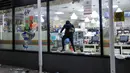 Seseorang membawa barang yang dijarah dari toko 7-Eleven di New York, AS (1/6/2020). Sejumlah toko di Amerika Serikat dijarah oleh pendemo yhang mengecam kematian warga kulit hitam George Floyd. (AP Photo/Frank Franklin II)