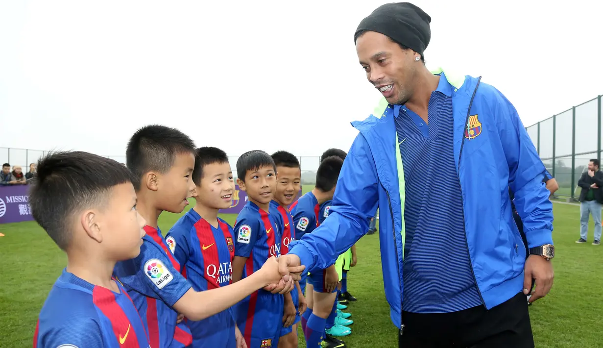Pemain sepak bola asal Brasil, Ronaldinho bersalaman dengan pemain bola cilik di China (24/2). Mantan pemain klub Spanyol, Barcelona itu menghadiri peresmian berdirinya akademi sepak bola Barcelona di China. (Handout / Mission Hills / AFP)