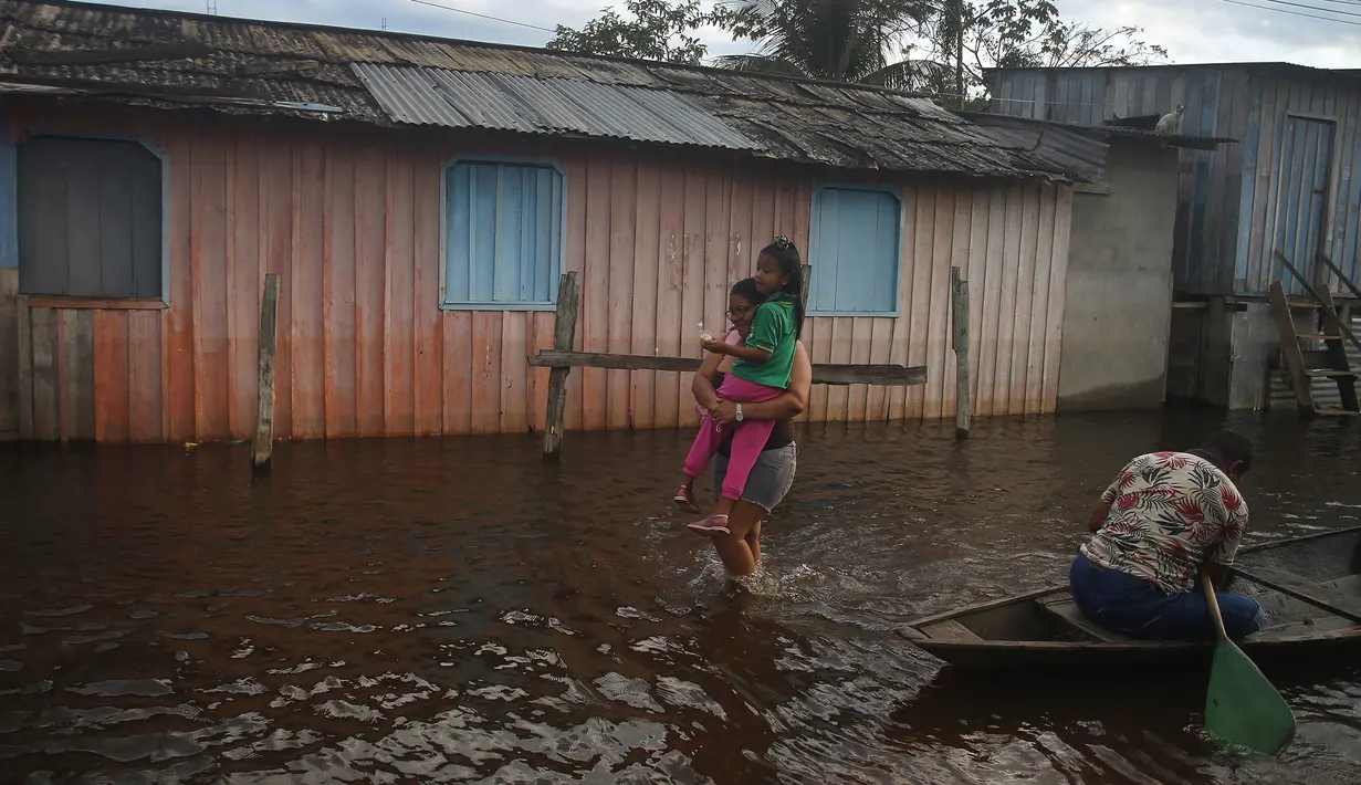 Seorang ibu membawa putrinya menuju sekolah di jalan yang tergenang banjir oleh naiknya sungai Negro di Iranduba, negara bagian Amazonas, Brasil, Senin (23/5/2022). Wilayah Amazon sedang dilanda banjir dengan 35 kotamadya yang menghadapi salah satu banjir terburuk mereka dalam beberapa tahun dan permukaan air diperkirakan akan meningkat selama beberapa bulan mendatang. (AP Photo/Edmar Barros)