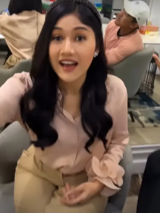 Ia kenakan blouse satin berwarna peach nude, dipadukan dengan celana cokelat dan belt hitam