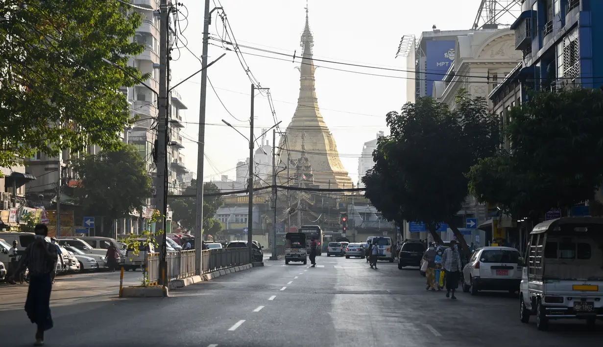 Orang-orang berjalan di sebelah Pagoda Shwedagon di jalan kosong di Yangon, Myanmar pada Senin (1/2/2021). Militer Myanmar mengumumkan satu tahun pemberlakuan situasi darurat setelah militer mengkudeta kekuasaan sipil. (STR/AFP)