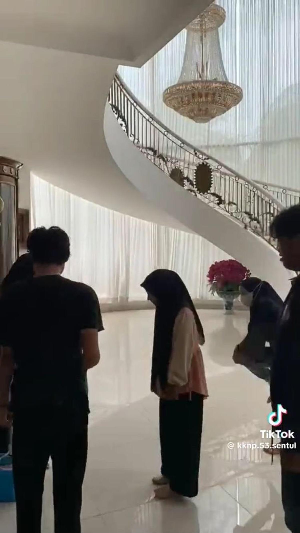 Rumah ini bahkan memiliki dua lantai. Bagian tangganya melingkar dan terdapat lampu gantung mewah di tengahnya. Persis seperti rumah-rumah mewah di sinetron.