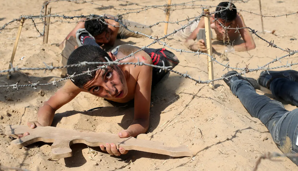 Seorang anak Palestina merangkak di bawah kawat berduri selama latihan militer di sebuah kamp musim panas yang diselenggarakan oleh Islamic Jihad Movement di Khan Younis di Jalur Gaza selatan (13/7). (REUTERS/Ibraheem Abu Mustafa)