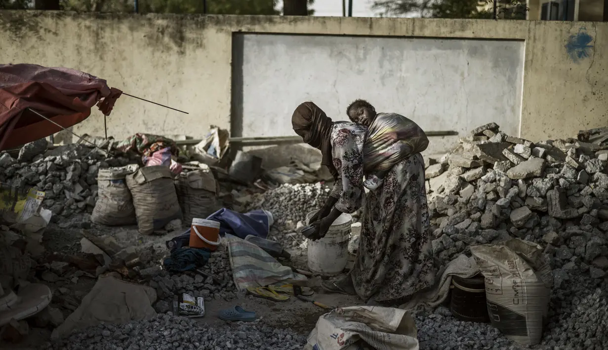 Seorang penghancur kerikil menggendong anaknya di antara lempengan dan batu yang lebih kecil dekat Cite International des Affaires, N'Djamena, Chad, 12 April 2021. Dalam debu dan panas, wanita Chad menghancurkan kerikil untuk memenuhi kebutuhan. (MARCO LONGARI/AFP)