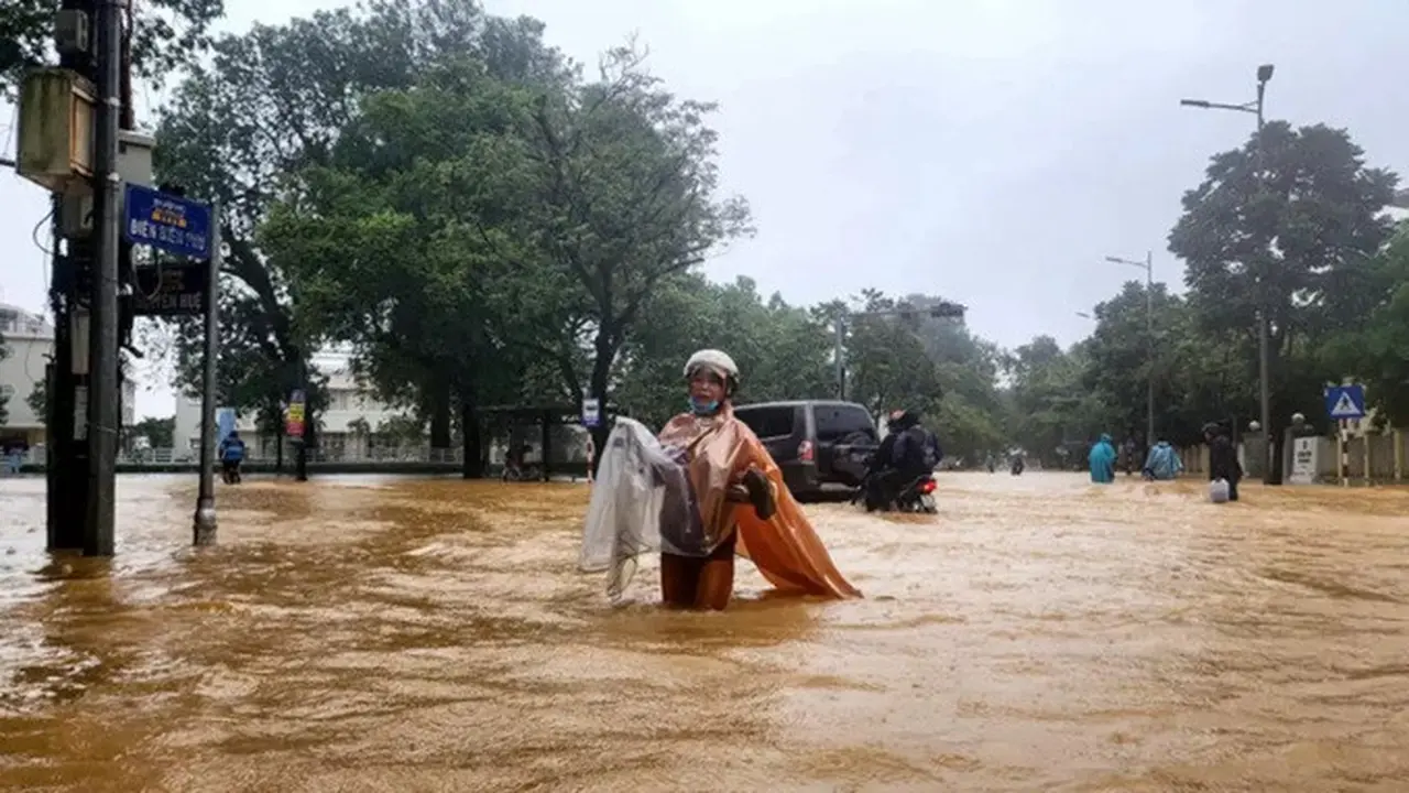 Seorang perempuan mengenakan jas hujan berjalan menembus banjir di Hue, Vietnam, pada Senin, (28/10/2025).