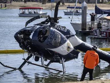 Sebuah derek digunakan untuk mengangkat helikopter Polisi Pantai Huntington di Pantai Newport, California (20/2/2022). Pihak berwenang sedang menyelidiki penyebab kecelakaan helikopter polisi di sepanjang pantai California Selatan tersebut. (Mindy Schauer/The Orange County Register via AP)