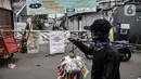 Pedagang melintas di depan jalan permukiman yang ditutup usai ditetapkan sebagai Zona Merah Covid-19 di RW 03 Kelurahan Kebon Manggis, Jakarta, Selasa (14/7/2020). Jumlah RW yang masuk dalam zona merah Covid-19 di DKI Jakarta kembali bertambah menjadi 30 RW. (Mmerdeka.com/Iqbal Nugroho)