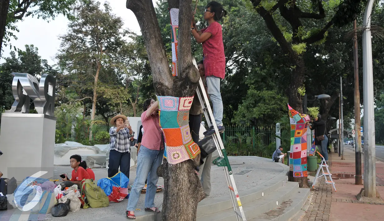 Seniman memasang rajutan kain di pohon dekat lokasi Taman Pandang Istana, Jakarta, Jumat (29/7). Penghiasan dilakukan jelang diresmikannya Taman Pandang Istana. (Liputan6.com/Yoppy Renato)