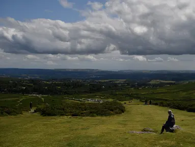 Seorang pejalan kaki memandang ke arah Torbay ketika mereka beristirahat di kaki Haytor Rocks di Taman Nasional Dartmoor, dekat Exeter, Inggris barat daya (12/8/2019). Dartmoor merupakan sebuah kawasan dataran tinggi di sebelah selatan Devon, Inggris. (AFP Photo/Ben Stansall)