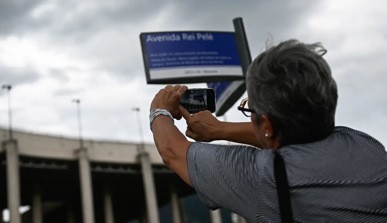 Seorang perempuan mengambil gambar tanda jalan bertuliskan "Avenue King Pele" di luar stadion Maracana di Rio de Janeiro, Brasil pada 4 Januari 2023. Balai Kota Rio de Janeiro secara resmi menamai jalan yang mengelilingi stadion Maracana Avenue Rei Pele (King Pele). (MAURO PIMENTEL/AFP)