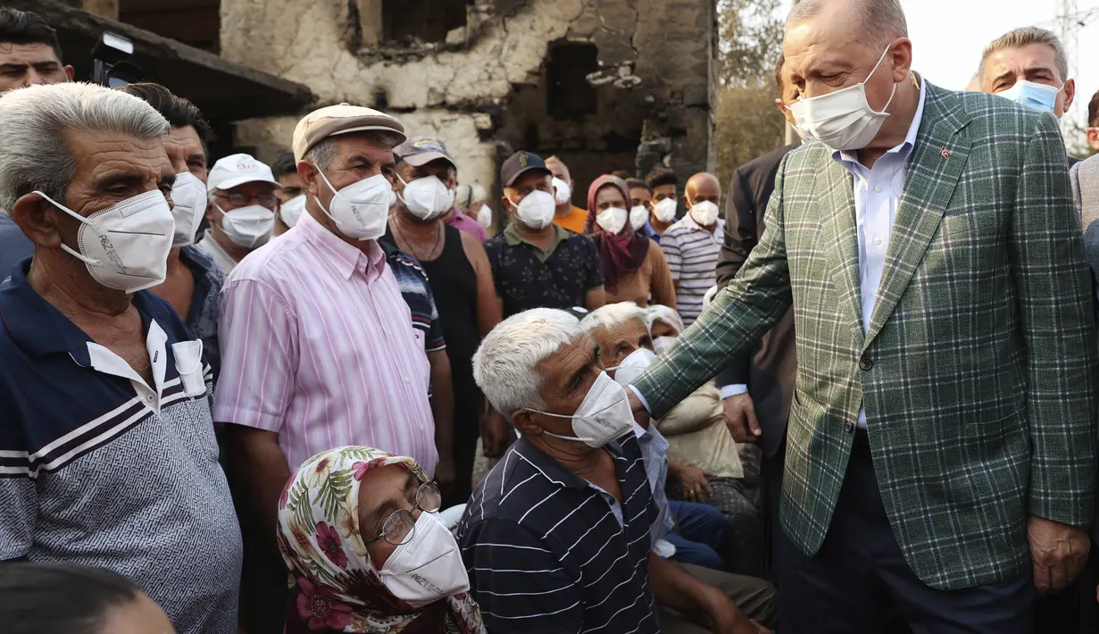 Presiden Turki Recep Tayyip Erdogan berbicara dengan penduduk desa di depan sebuah rumah yang hancur akibat kebakaran hutan di Manavgat, Antalya, Turki, Sabtu (31/7/2021). (Turkish Presidency via AP, Pool)