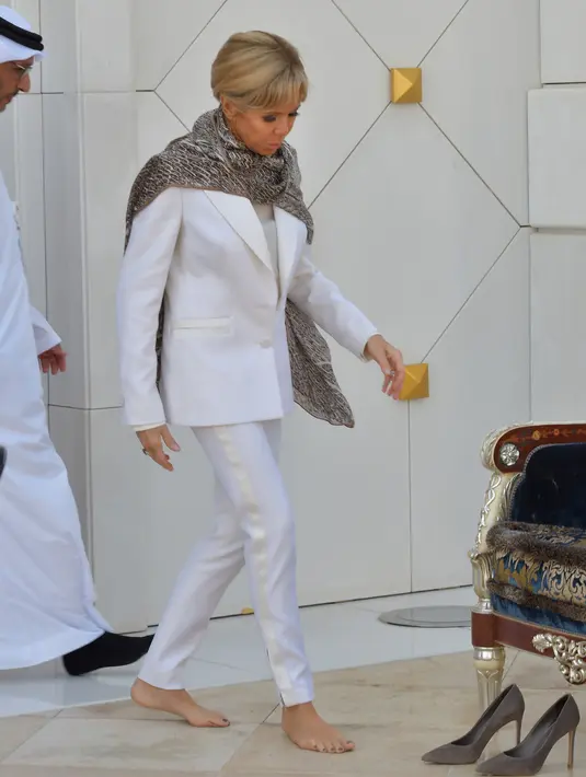 Istri Presiden Prancis, Brigitte Macron memakai sepatu seusai mengunjungi Masjid Sheik Zayed di Abu Dhabi, Uni Emirate Arab, Kamis (9/11). Di masjid itu, Brigitte mengenakan penutup kepala bermotif leopard dan melepas sepatu. (Giuseppe CACACE / AFP)