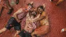 Orang-orang yang bersuka ria berbaring di genangan tomat yang tergencet selama "Tomatina" tahunan, pesta pertarungan tomat di desa Bunol dekat Valencia, Spanyol, Rabu (31/8/2022). Biasanya pertempuran berlangsung selama satu jam, setelah sebagian besar area di alun-alun kota penuh dengan tomat. (AP Photo/Alberto Saiz)